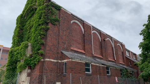 An abandoned church with the windows covered and ivy over the front 
