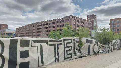 A wrap stating "Better Together" on a fence around an overgrown lot