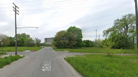 Vacant lots with grass and trees with an old train station in the distance